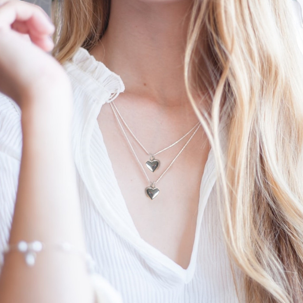 Two silver heart necklaces on a woman's neckline with a white blouse