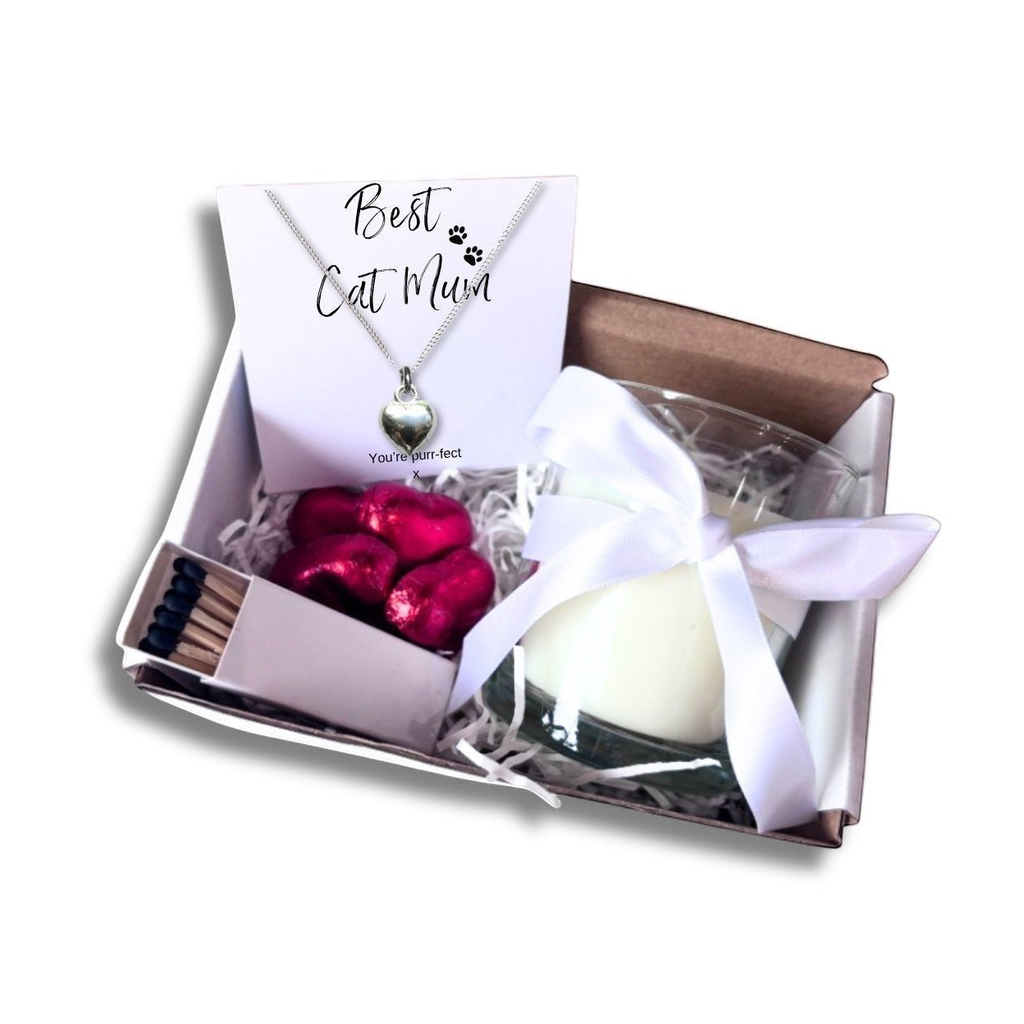 Open gift hamper with heart necklace, white candle, red chocolates, and satin ribbon bow