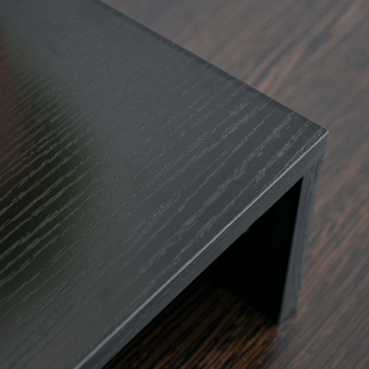 Close-up of dark monitor stand riser edge and textured board surface