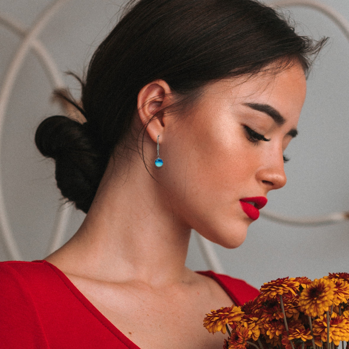Blue round drop earring with silver hook on a woman’s ear