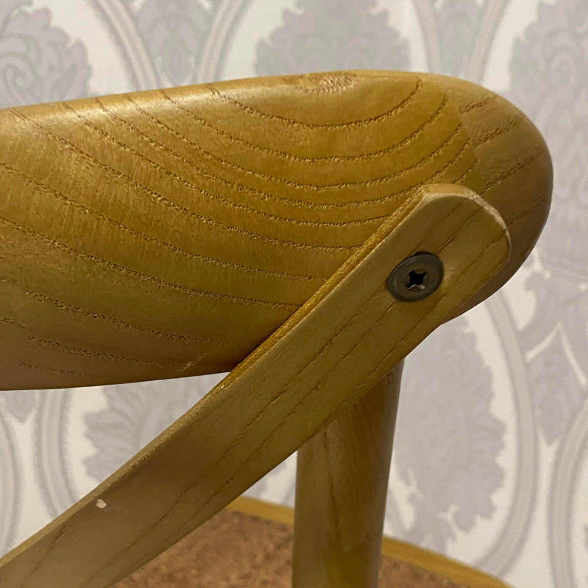 Woven fabric upholstered seat/back edge with wood arm and slotted screw, warm oak.