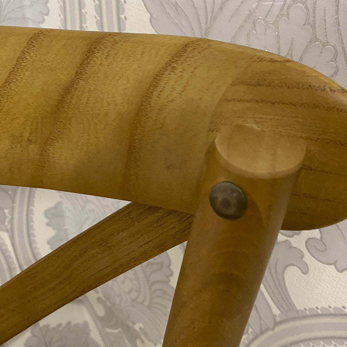 Wooden chair back post and arm with round metal fastener, warm oak finish.